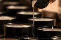 Hot wax poured from a metal pitcher into rows of matte black vessels